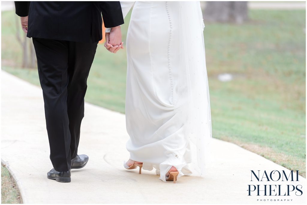 Bride and groom holding hands and walking towards their reception hall.