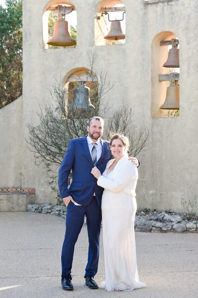 Newlyweds smiling in front of a wall of bells at Chapel Dulcinea, a small wedding venue in Austin TX.