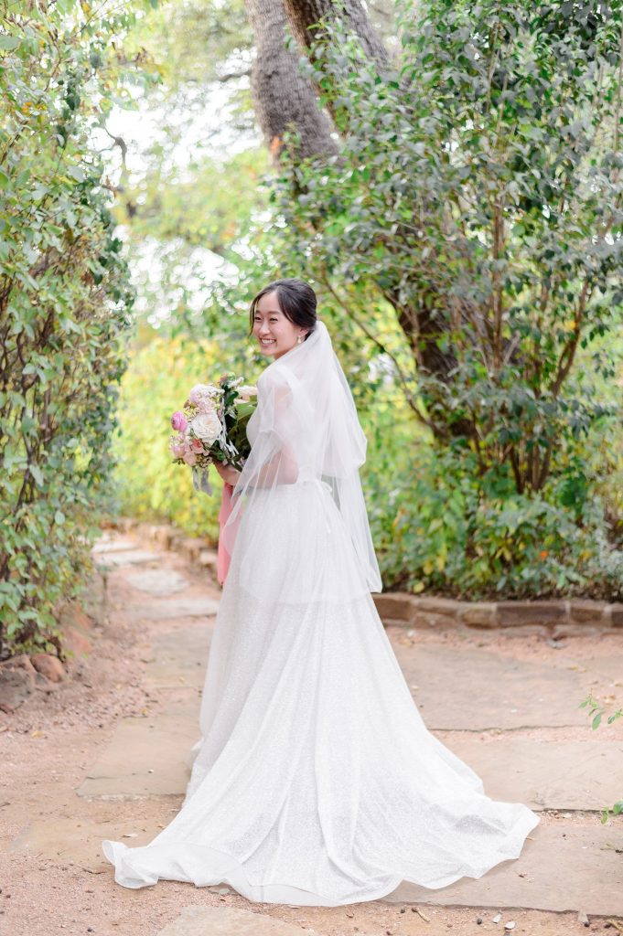 Bride looking over her shoulder smiling with a bouquet of pink flowers.