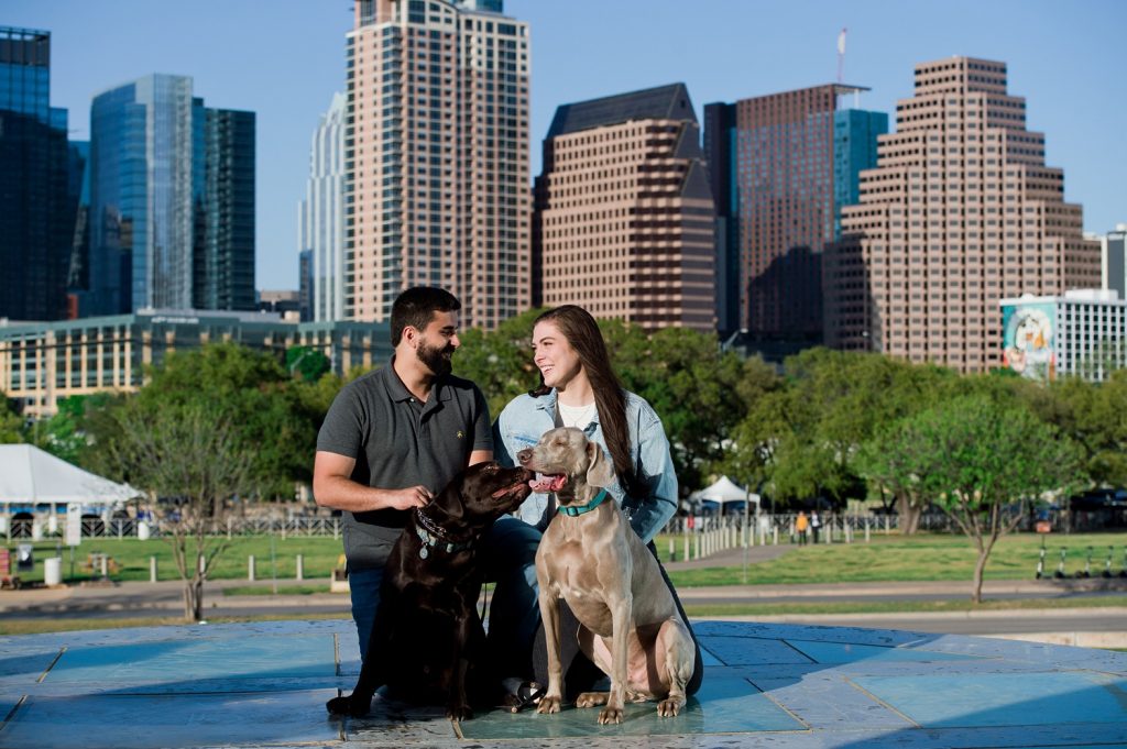 Engaged couple and their two dogs posing in front of the downtown Austin skyline.
