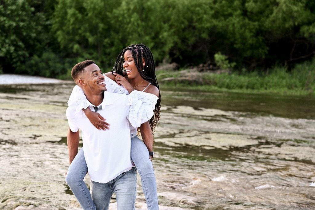 Woman on her fiancé's back at McKinney Falls State Park for engagement photos in Austin, TX.