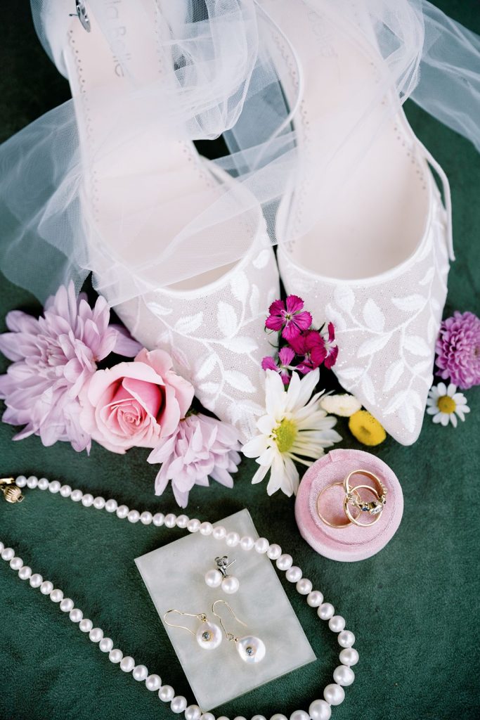 Flat lay of bridal shoes, jewelry, and flowers.