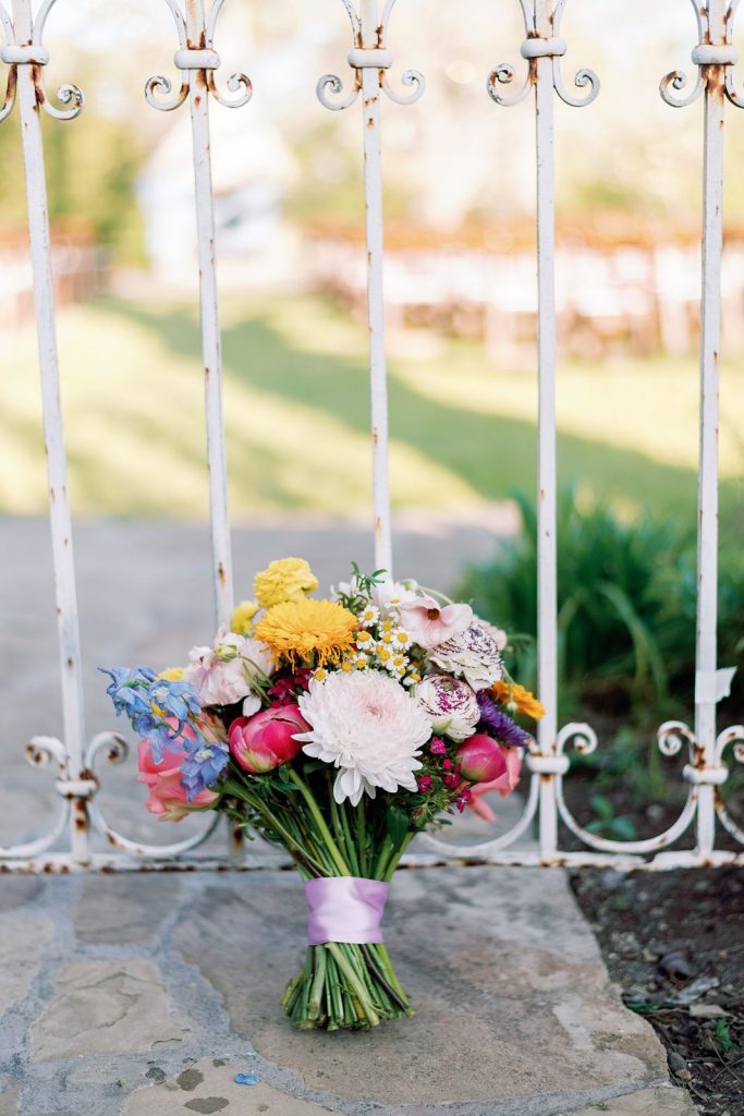 Colorful bridal bouquet leaning against antique gate at Pecan Springs Ranch Austin wedding venue.
