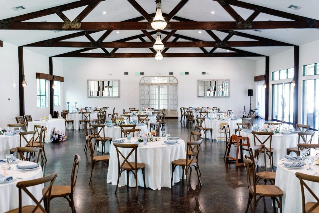 Wide shot of Pecan Springs Ranch wedding reception space with guest tables and crossback chairs.