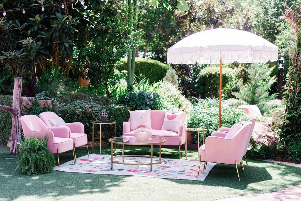 Pink lounge furniture and umbrella set up in the garden at The Hummingbird House, a small wedding venue in Austin TX.