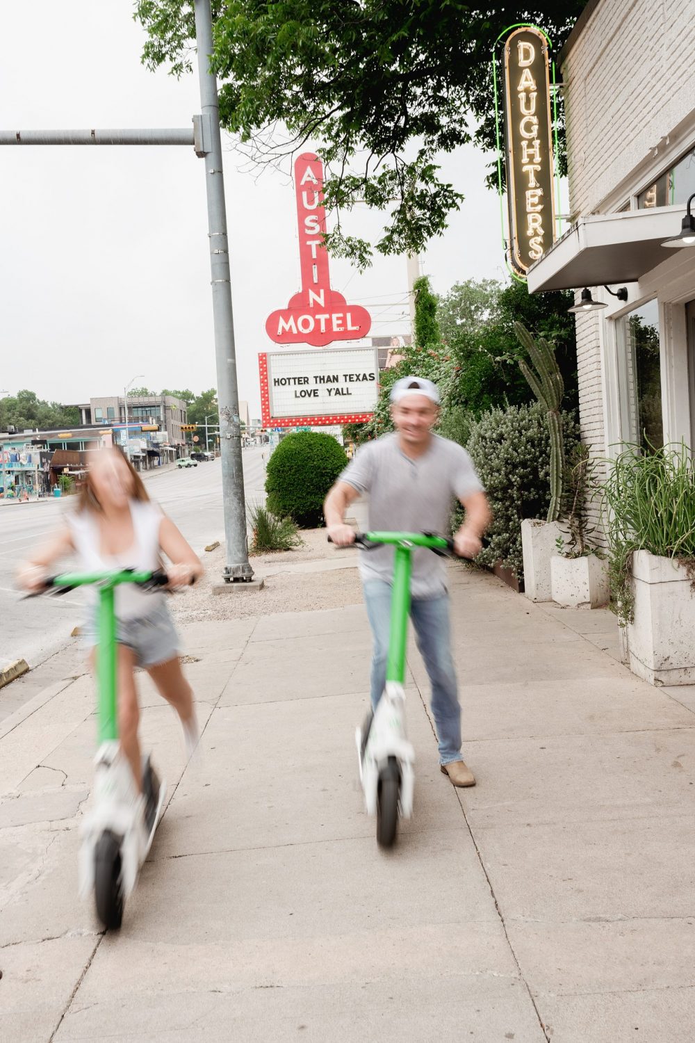 Couple riding scooters in front of the Austin Motel sign