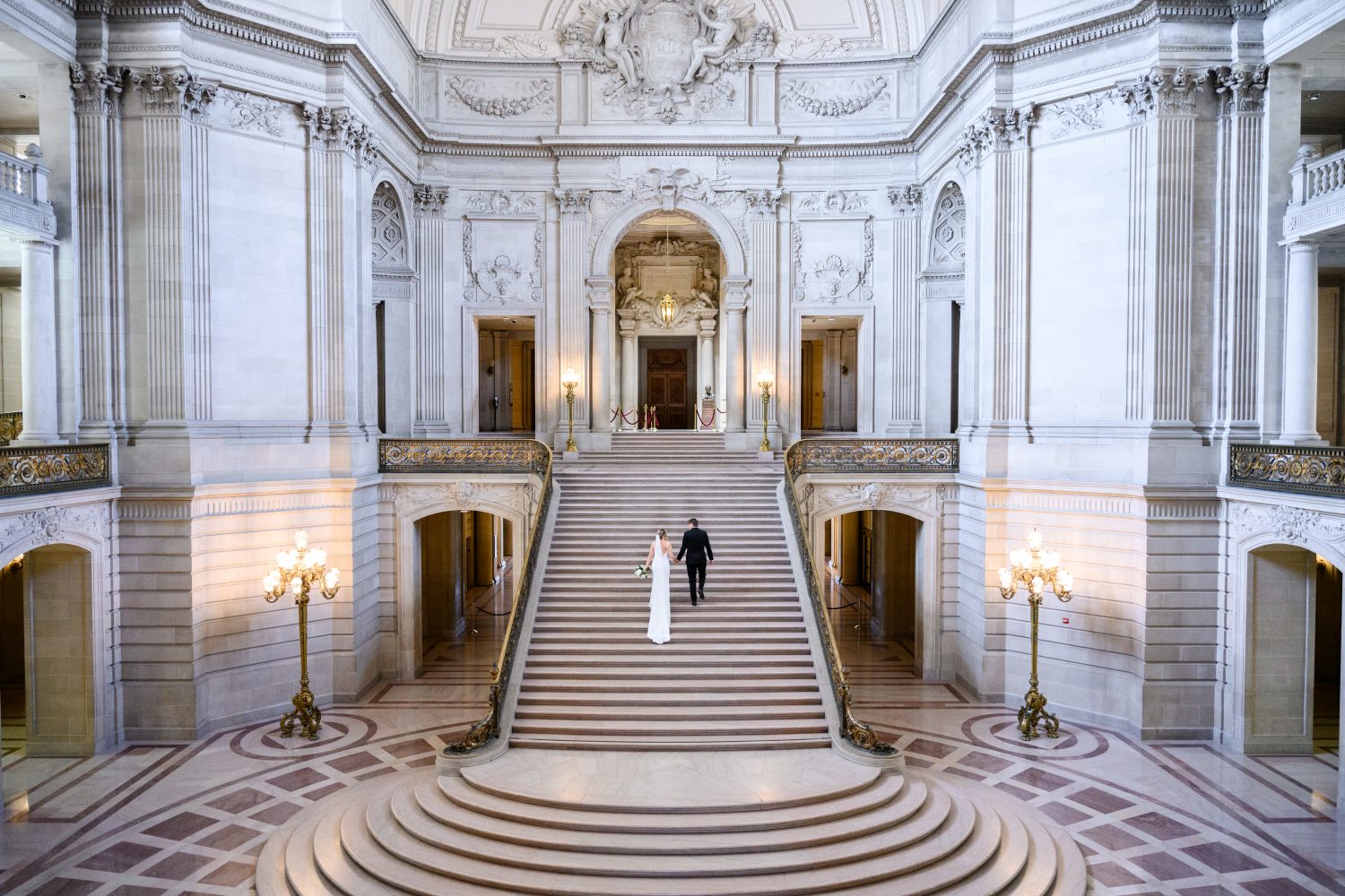 Bride and groom walking up large staircase in San Francisco city hall