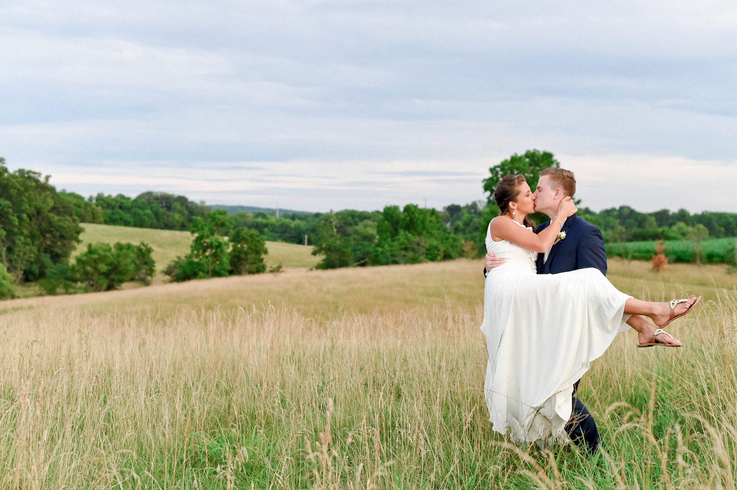 Groom holding bride and kissing in a field in Virginia at destination elopement
